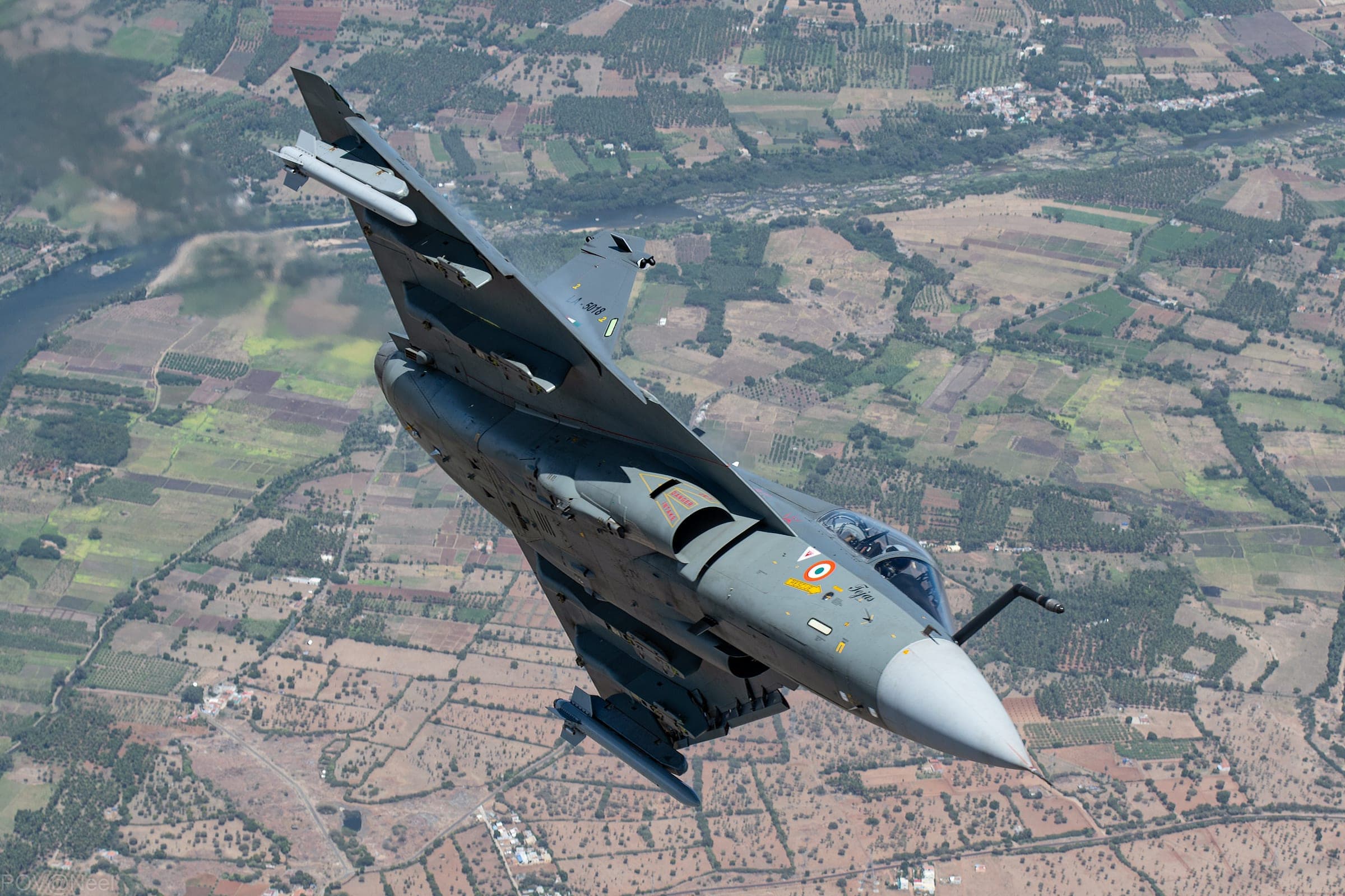 An Indian Air Force Tejas fighter diving over farmland