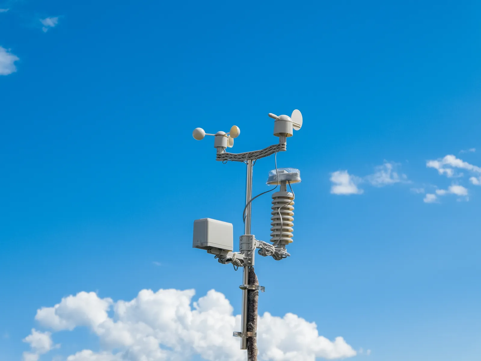 Automatic weather station with wind and rain sensors against a blue sky