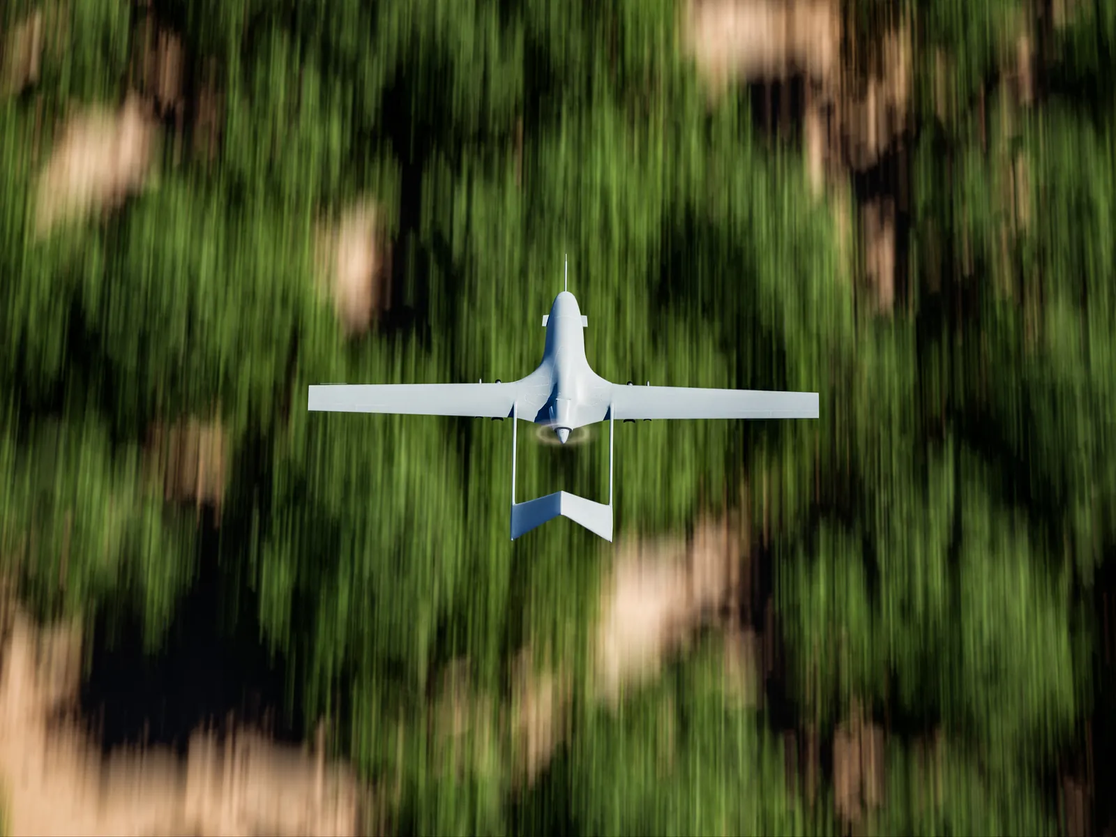 Fixed-wing military drone flying over a forest